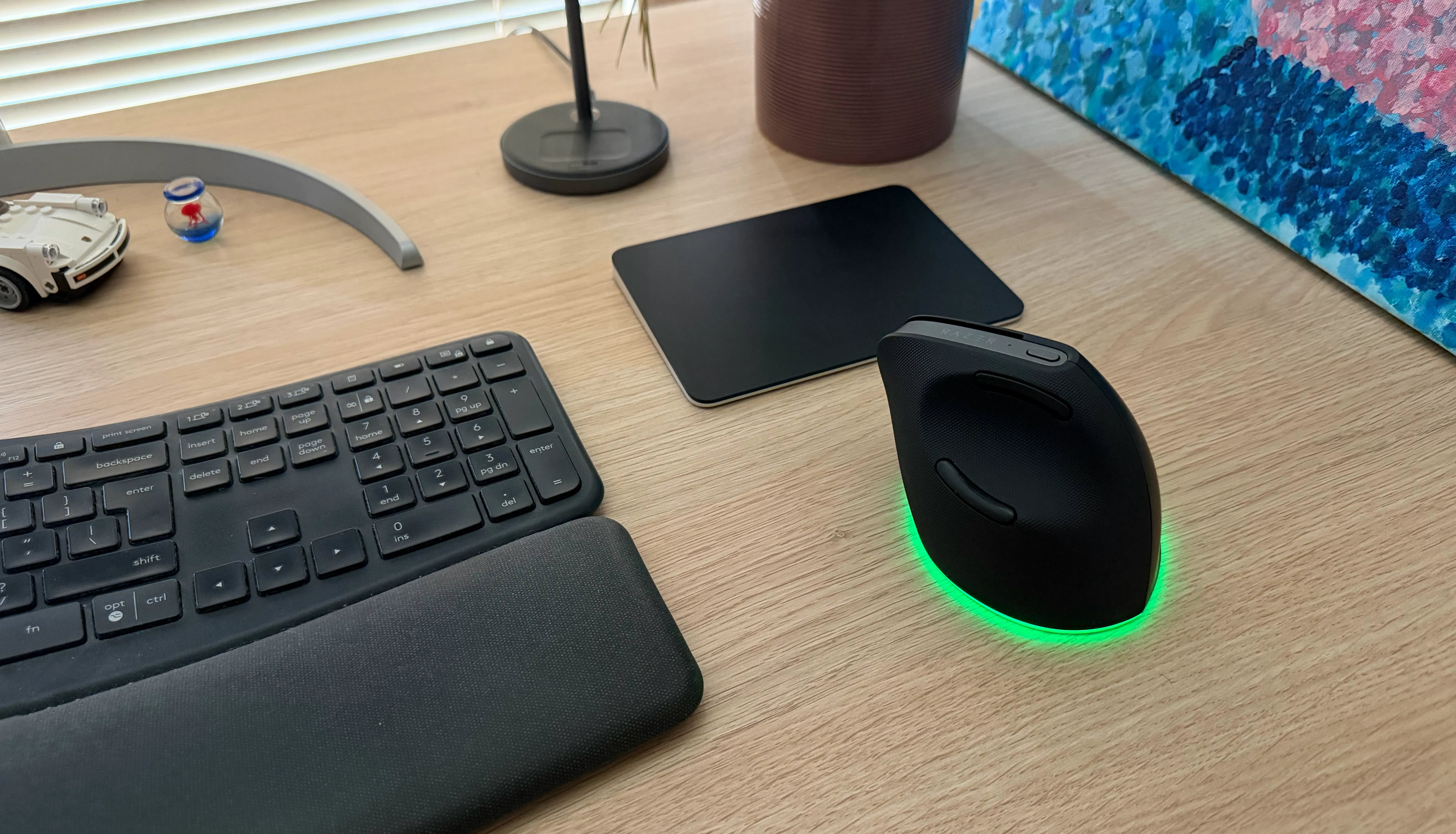 A black Magic Trackpad and Razer vertical mouse beside a keyboard on a wooden desk